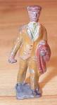 Collectible antique toy soldier type of toy of a male walking carrying a coat over one arm. His other hand is slightly curved upwards in a manner that makes us think that he might originally have been...