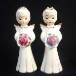 A pair of pretty ceramic angel figurines from 1950s Japan. They're slender with short curly platinum blond hair and hold nosegays or bouquets of mauve-purple flowers. Their long white gowns, little wi...