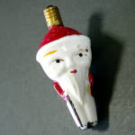 This odd looking Japan Santa C6 milk glass Christmas light bulb has a pointy cone head with a long Fu Manchu style beard that comes to a sharp point, ending at the knees. Santa is carrying a staff or ...