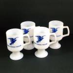 A set of four circa 1970s milk glass pedestal mugs, decorated on the fronts with a stylized American Eagle and the words Power Courage Freedom. Oddly enough, the backs of the mugs have four different ...