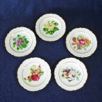 A set of five porcelain ceramic scalloped butter pat plates from Japan, just 3-1/2 inches diameter. Each is trimmed in gold and has a different flower decal decoration: hibiscus, violets, pansies, ros...