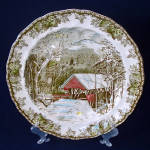 This English transferware chop plate or round serving platter is in the popular Friendly Village pattern, produced in England from 1953 to 2003. The covered bridge scene platter measures 12-1/2 inches...