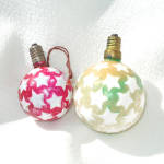 A pair of embossed star-covered ball figural milk glass Christmas light bulbs in two different colors and sizes. The smaller one is 2" tall, red with white stars and does not light. It's been con...
