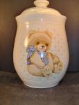 Tienshan Stoneware Country Bear Cookie Jar, very light tan with a sitting tan bear wearing a white polka dotted blue bow. There is a blue and pink design behind the bear. The lid has a blue design wit...